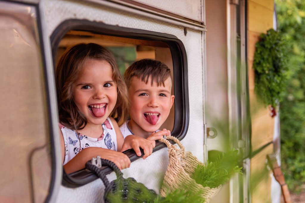 Children look out of their trailer window. Brother sister are resting with their parents in camping